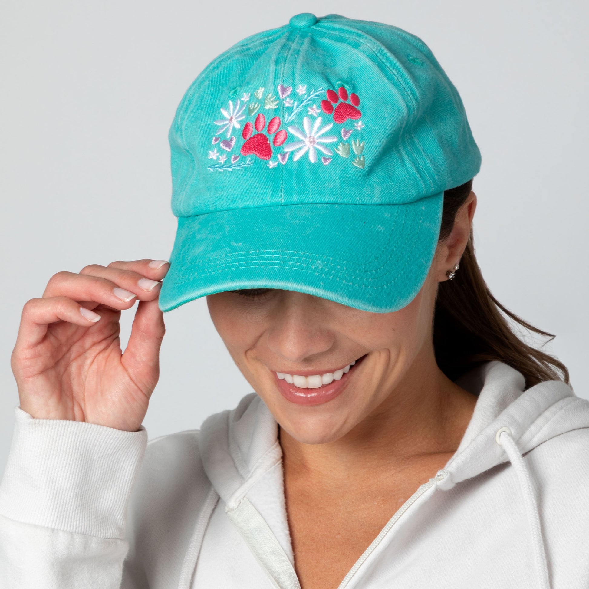 Turquoise cap with floral and paw print design worn by a person on a gray background