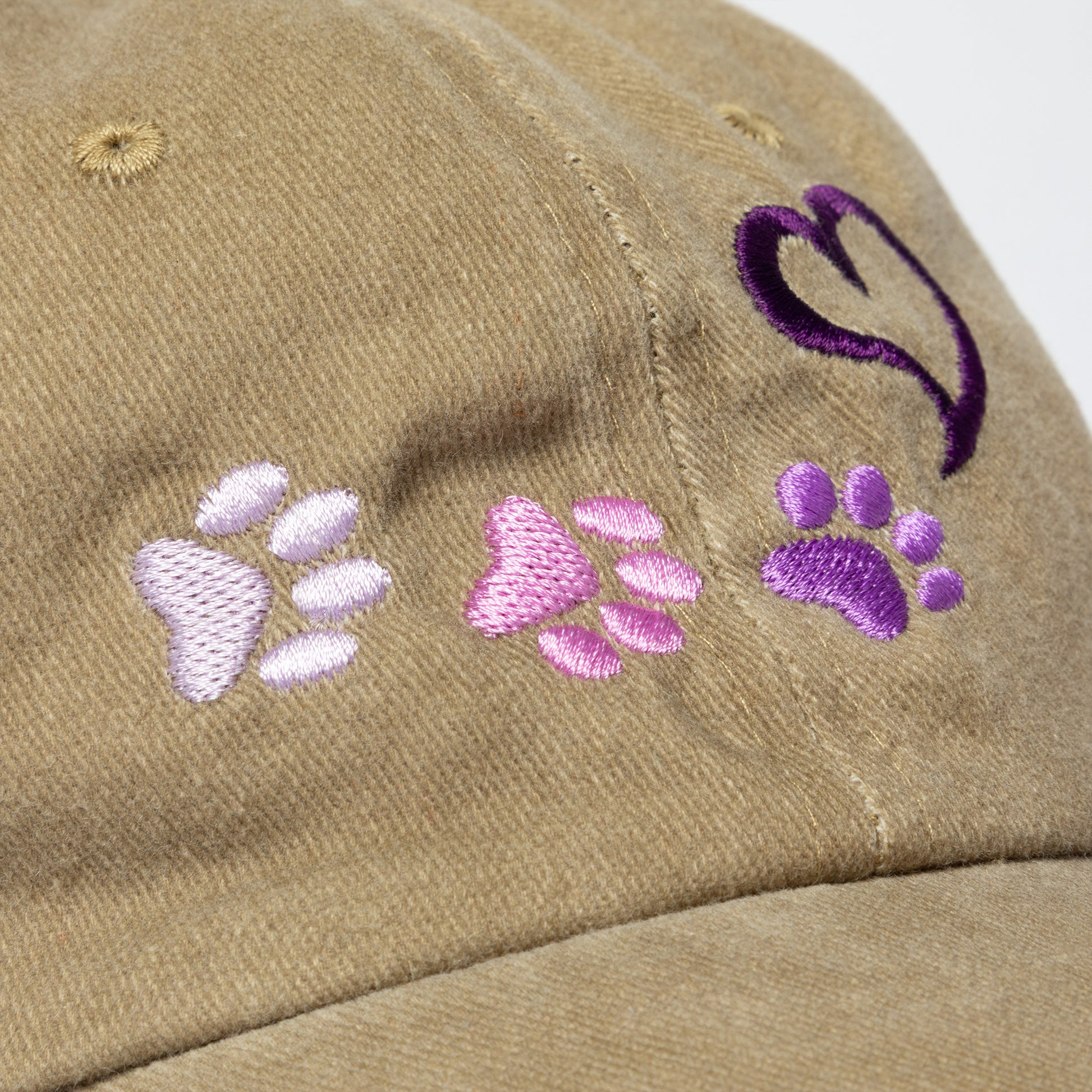 Tan cap with embroidered paw prints in purple and pink on a white background