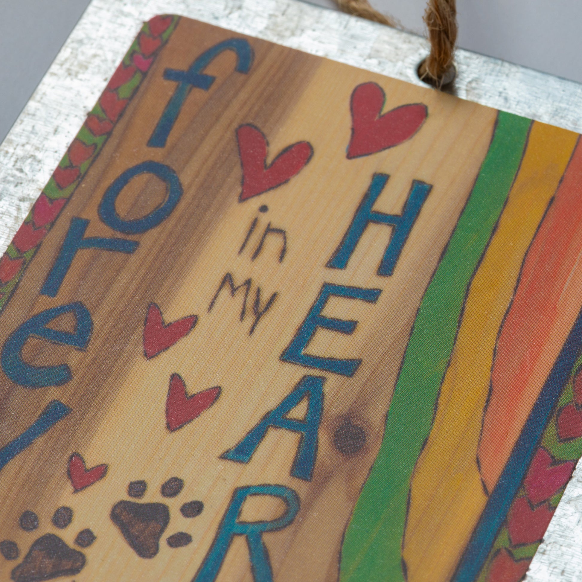 "Forever in My Heart" text on a wood background with a heart border on both sides with a rainbow design and paw prints against a white background