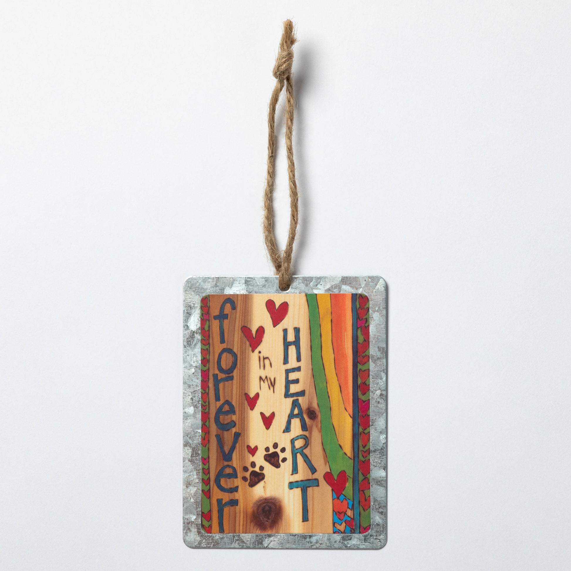 Decorative hanging ornament with "Forever in My Heart" text, hearts and paw prints on a wood background with a heart border on both sides with a rainbow design against a white background