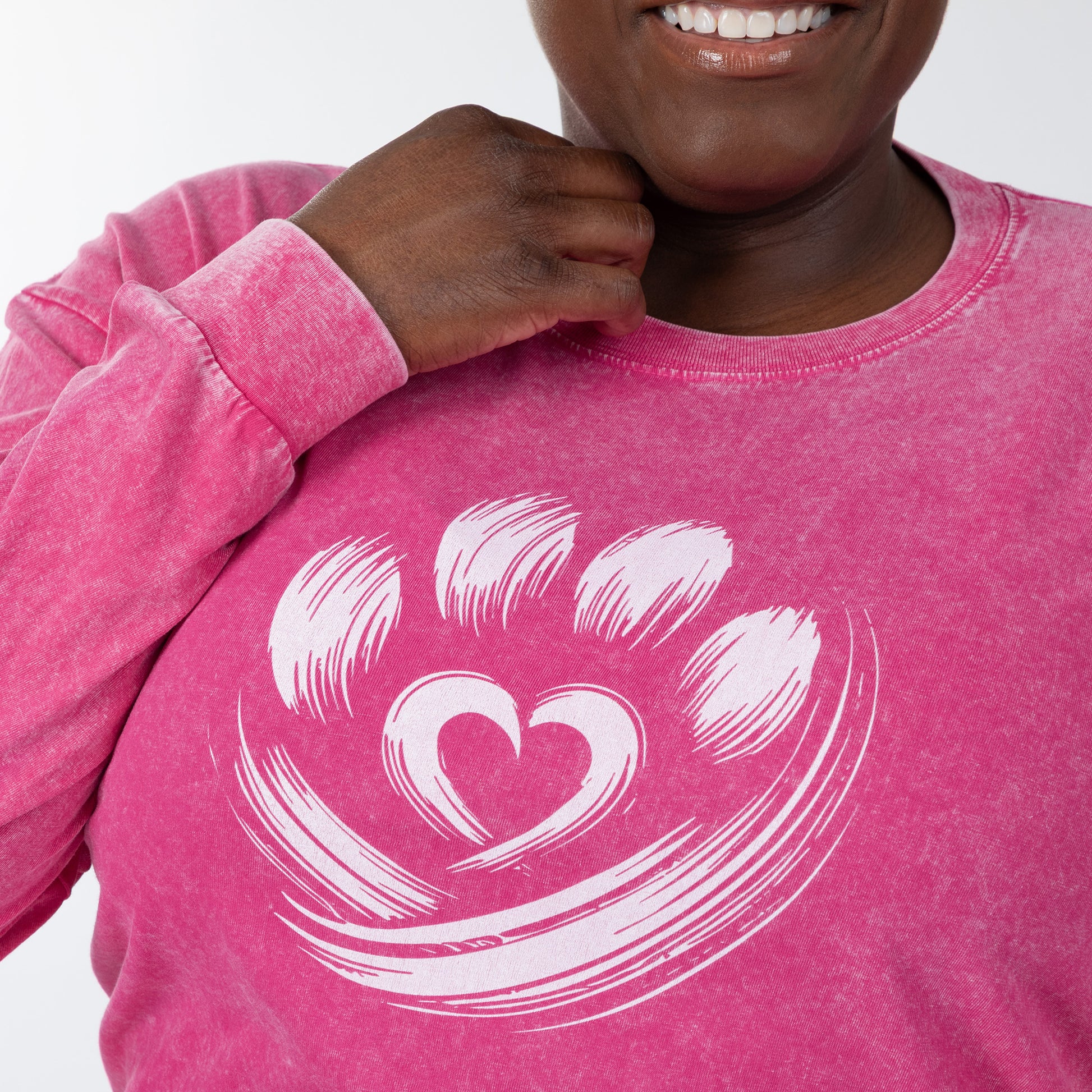 Person wearing a pink long sleeve tee with a white heart design on a plain background