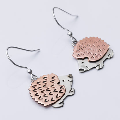 Hedgehog-shaped earrings in copper and silver on a light gray background