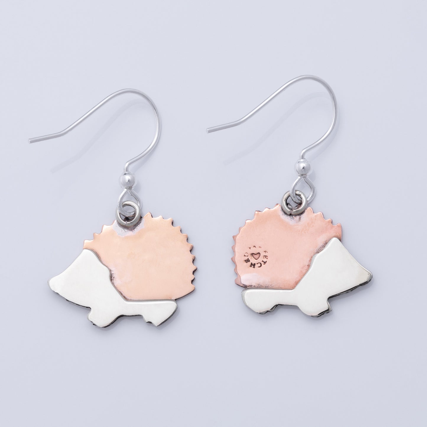 The back of a pair of hedgehog-shaped earrings with copper and silver designs on a light gray background