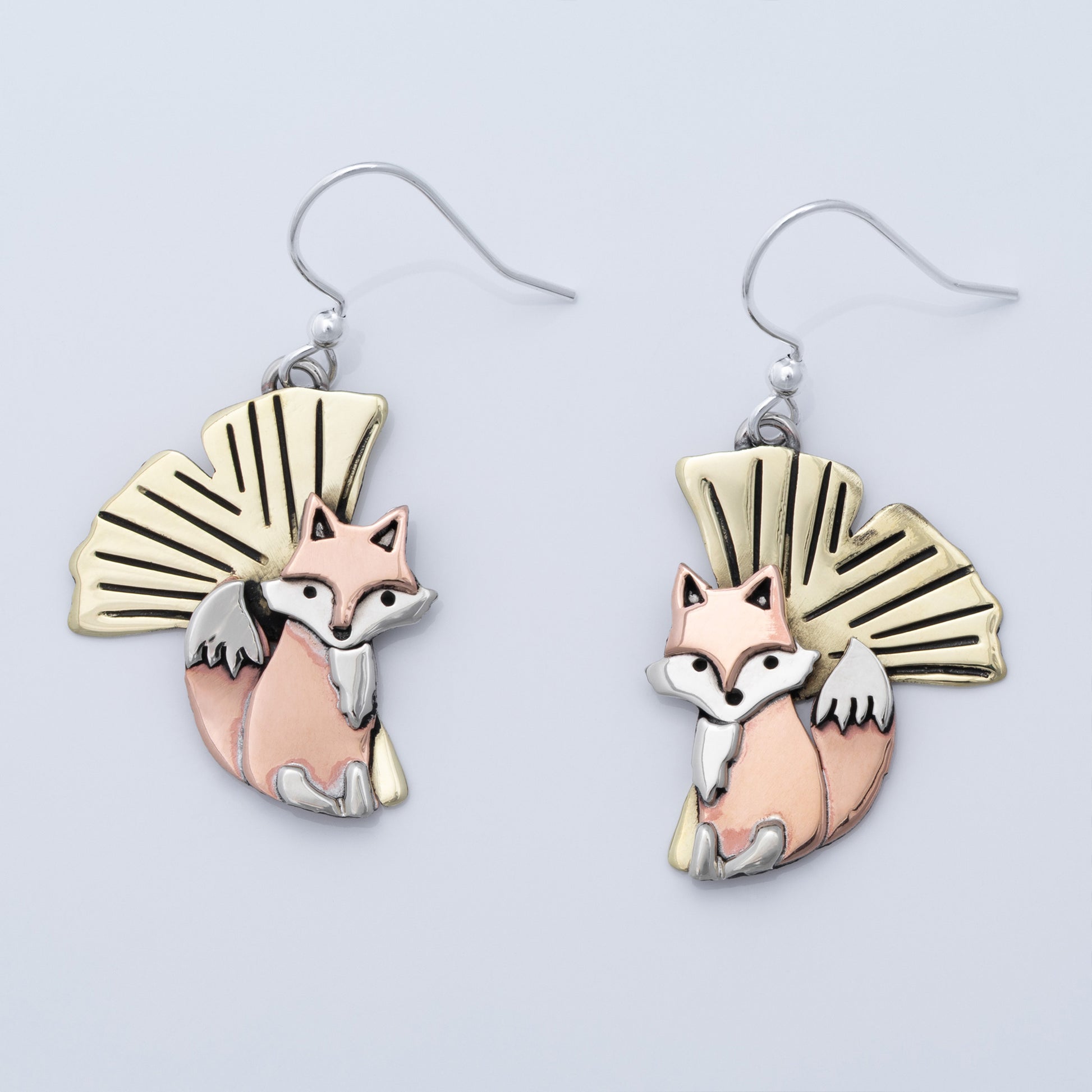 Pair of fox-themed earrings with brass, copper, and silver accents on a light gray background