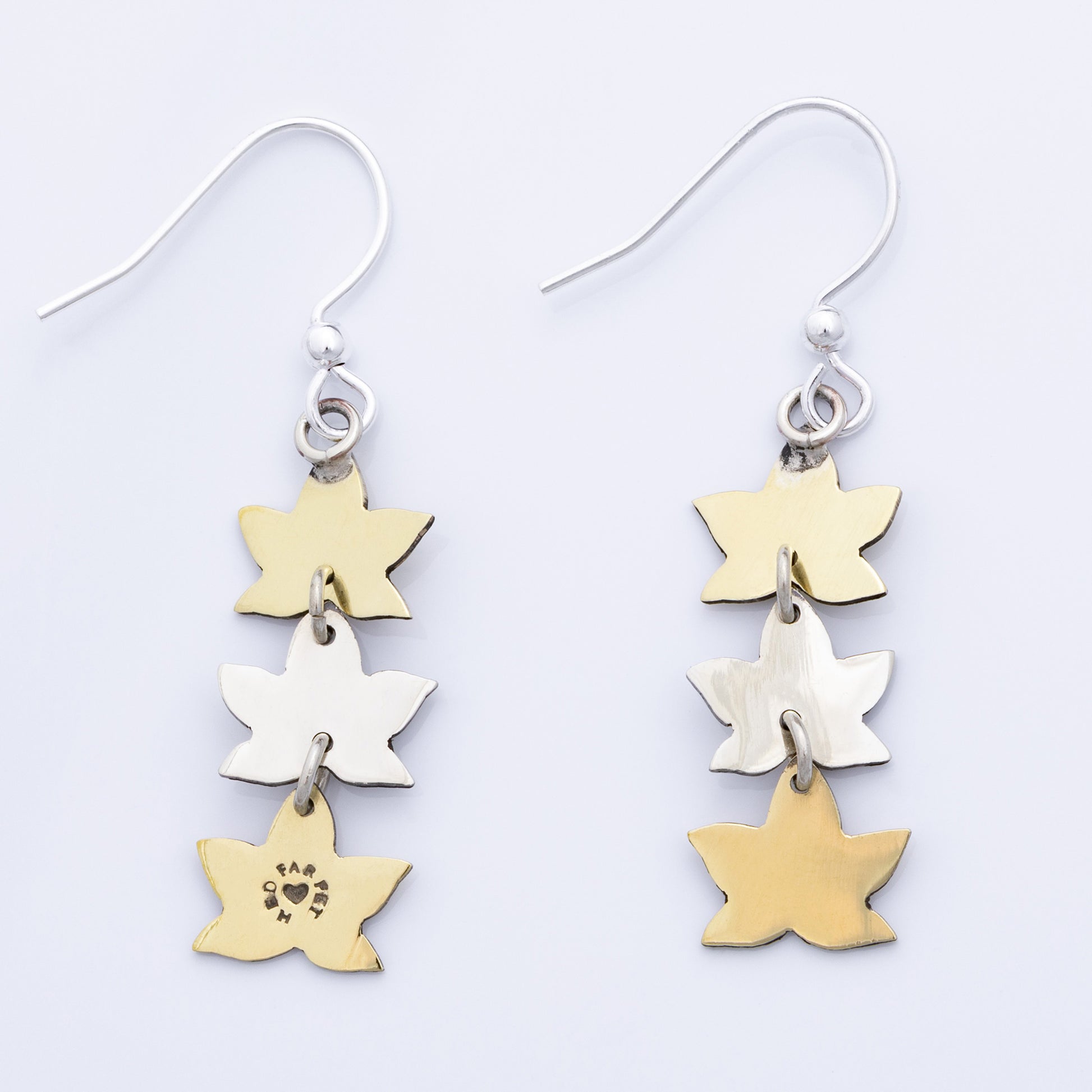 Backs of leaf-shaped earrings in gold and silver on a light gray background