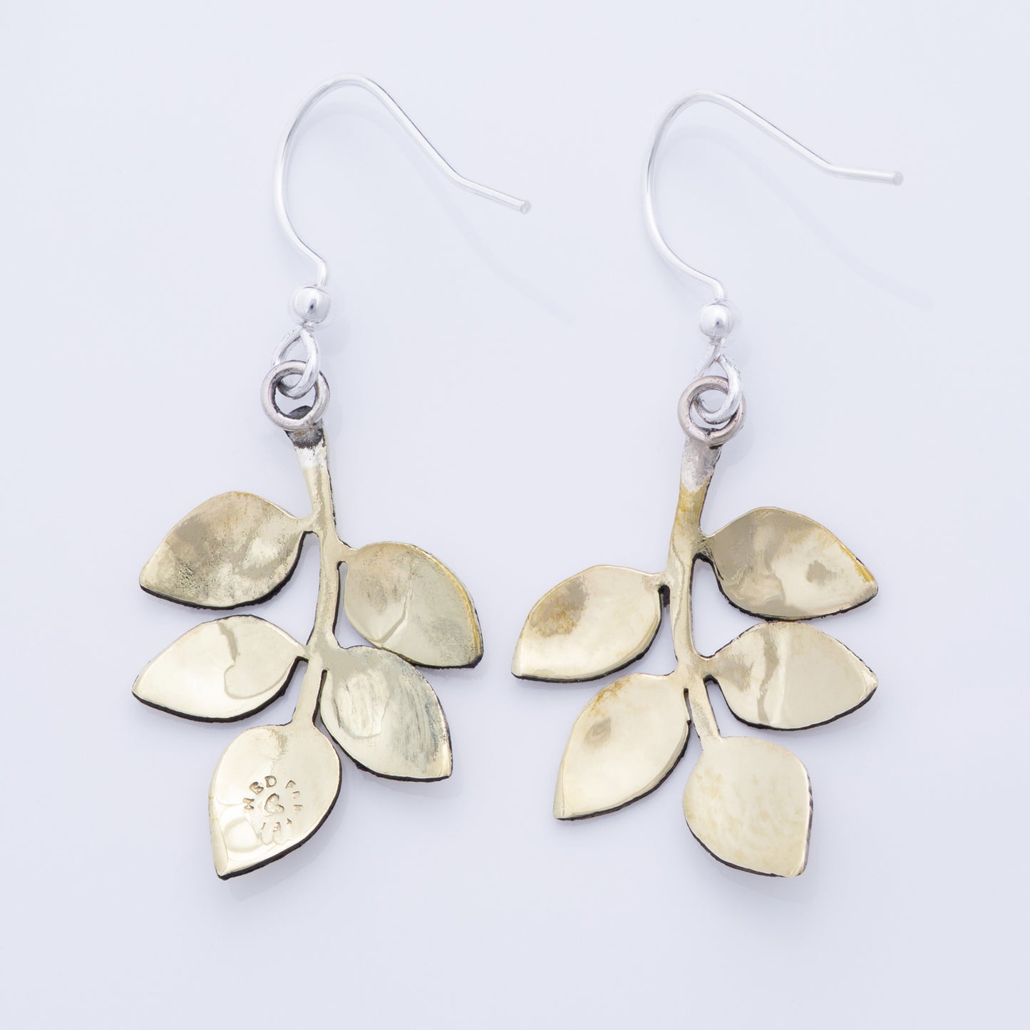 The backs of brass leaf-shaped earrings on a white background