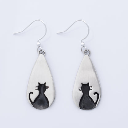 Teardrop-shaped silver earrings with black cat designs on a white background
