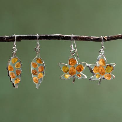 Pair of leaf-shaped earrings with autumn leaf design on a branch against a green background