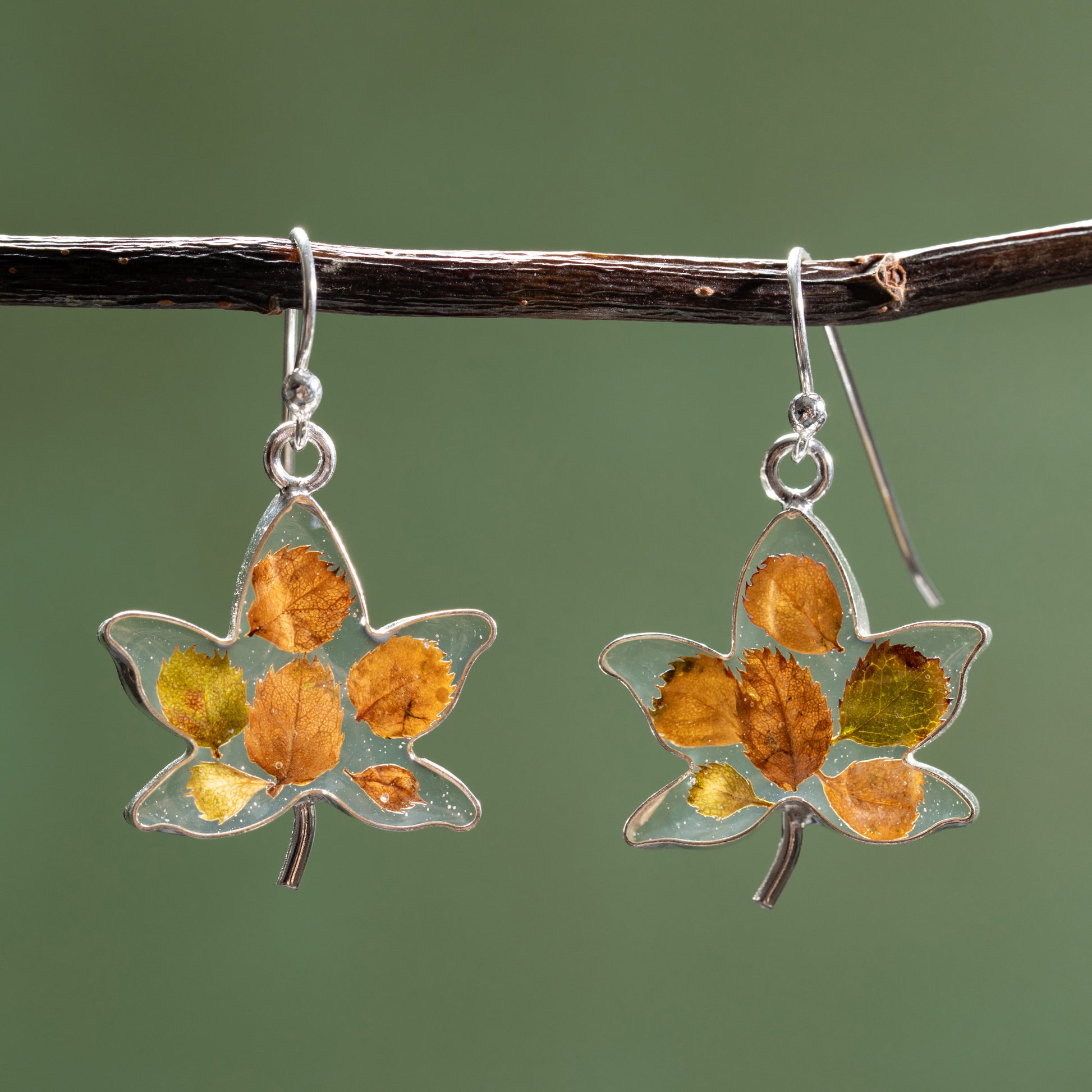 Maple leaf-shaped earrings with tiny leaves in resin on a branch against a green background