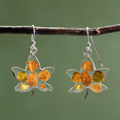 Maple leaf-shaped earrings with tiny leaves in resin on a branch against a green background