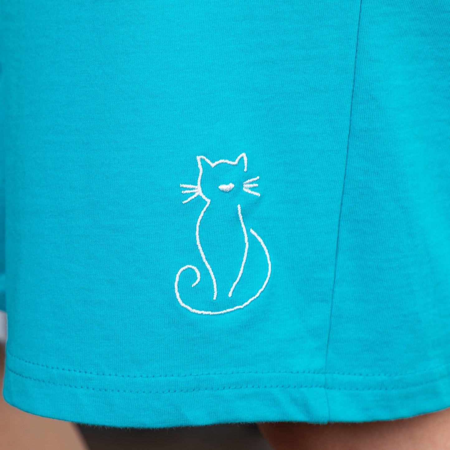Close-up of teal shorts with a white cat embroidery.