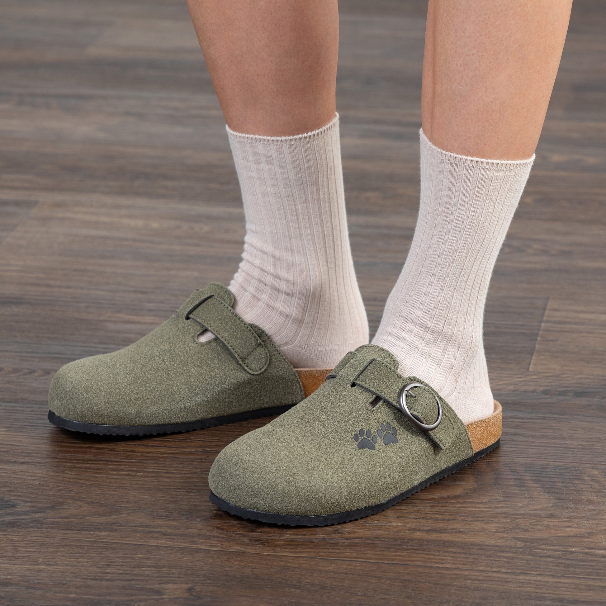 Person wearing green clogs with white socks on a wooden floor.