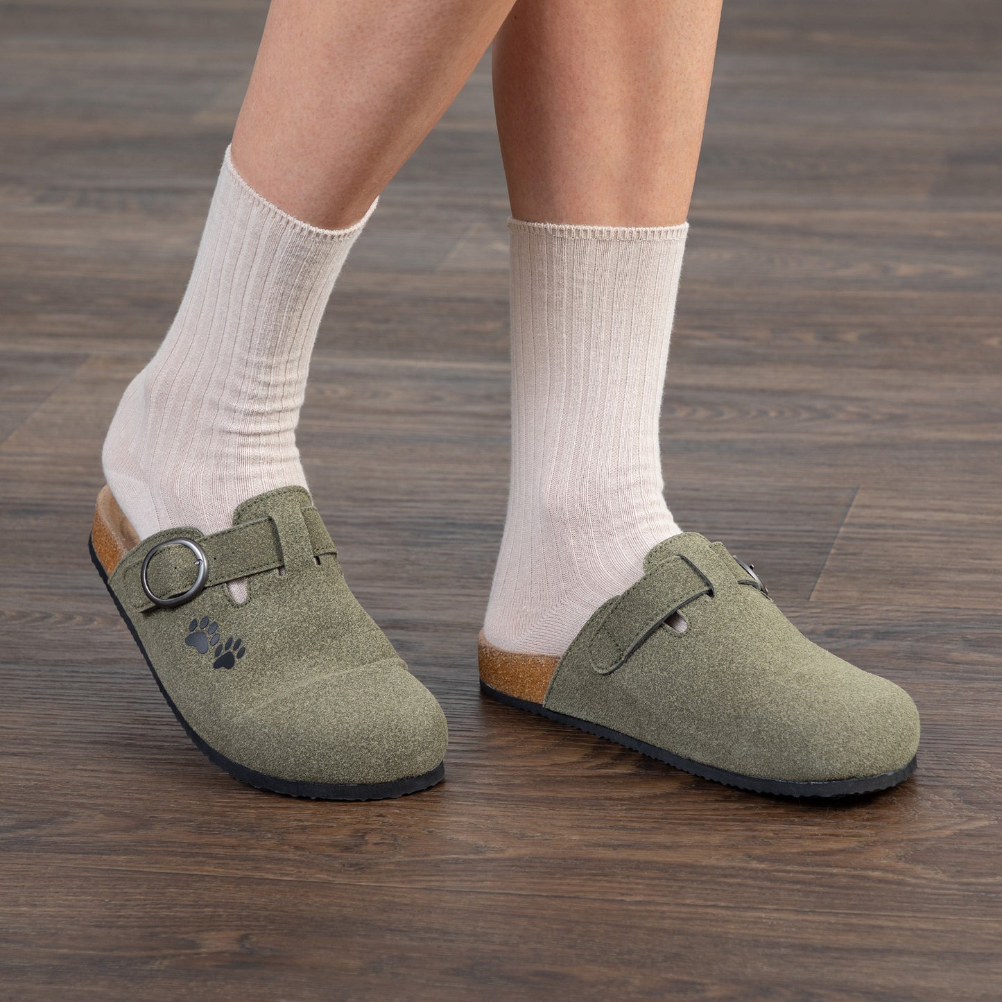 Person wearing green clogs with white socks on a wooden floor.