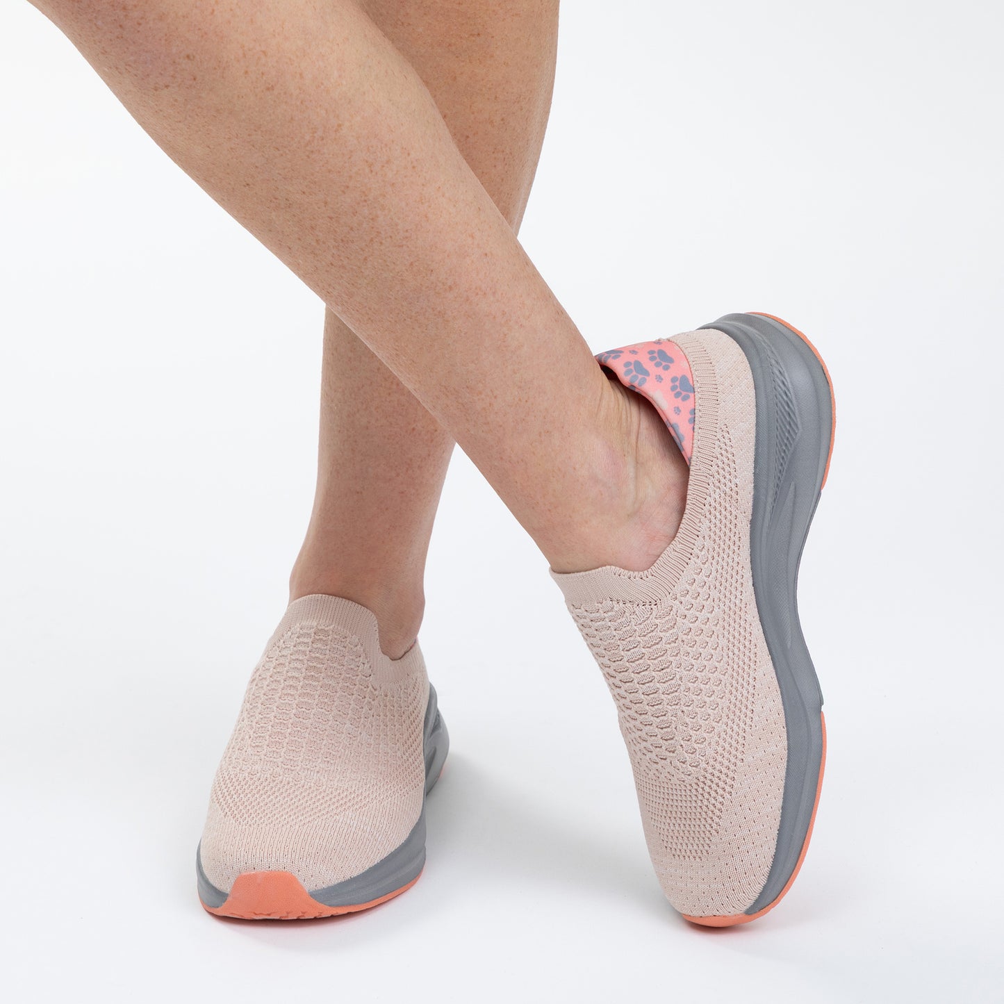 Light pink slip-on shoes with gray soles and orange accents worn by a person on a white background