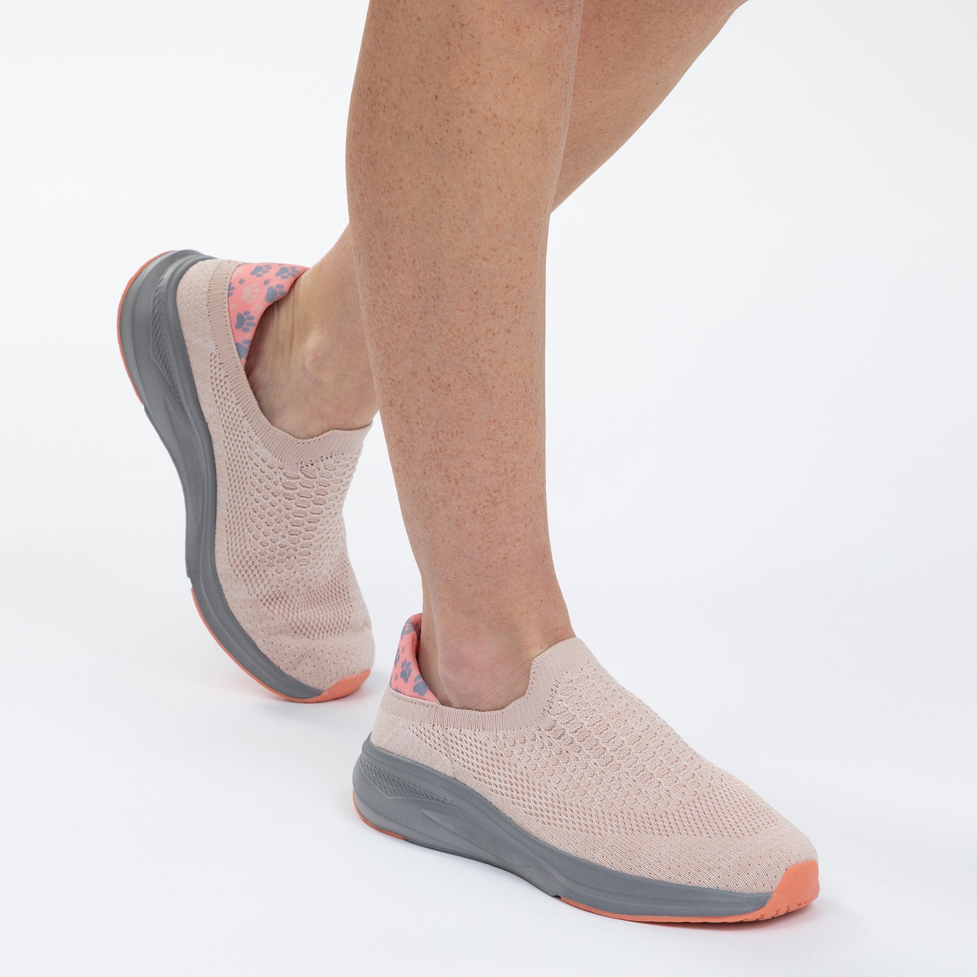 Light pink slip-on shoes with gray soles worn by a person on a white background