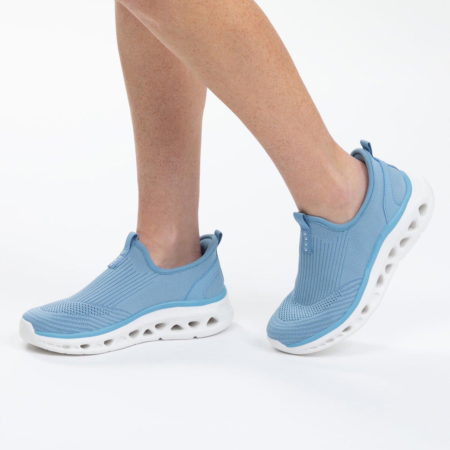Blue slip-on sneakers worn by a person on a white background
