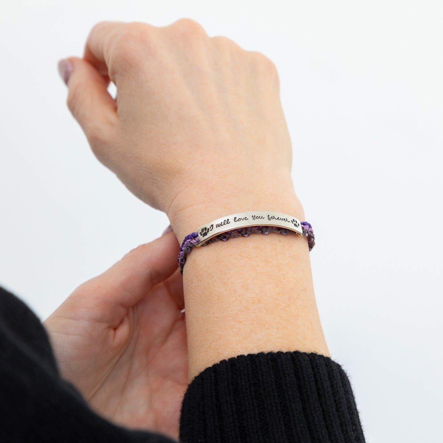 Hand wearing a purple bracelet with engraved text on a white background