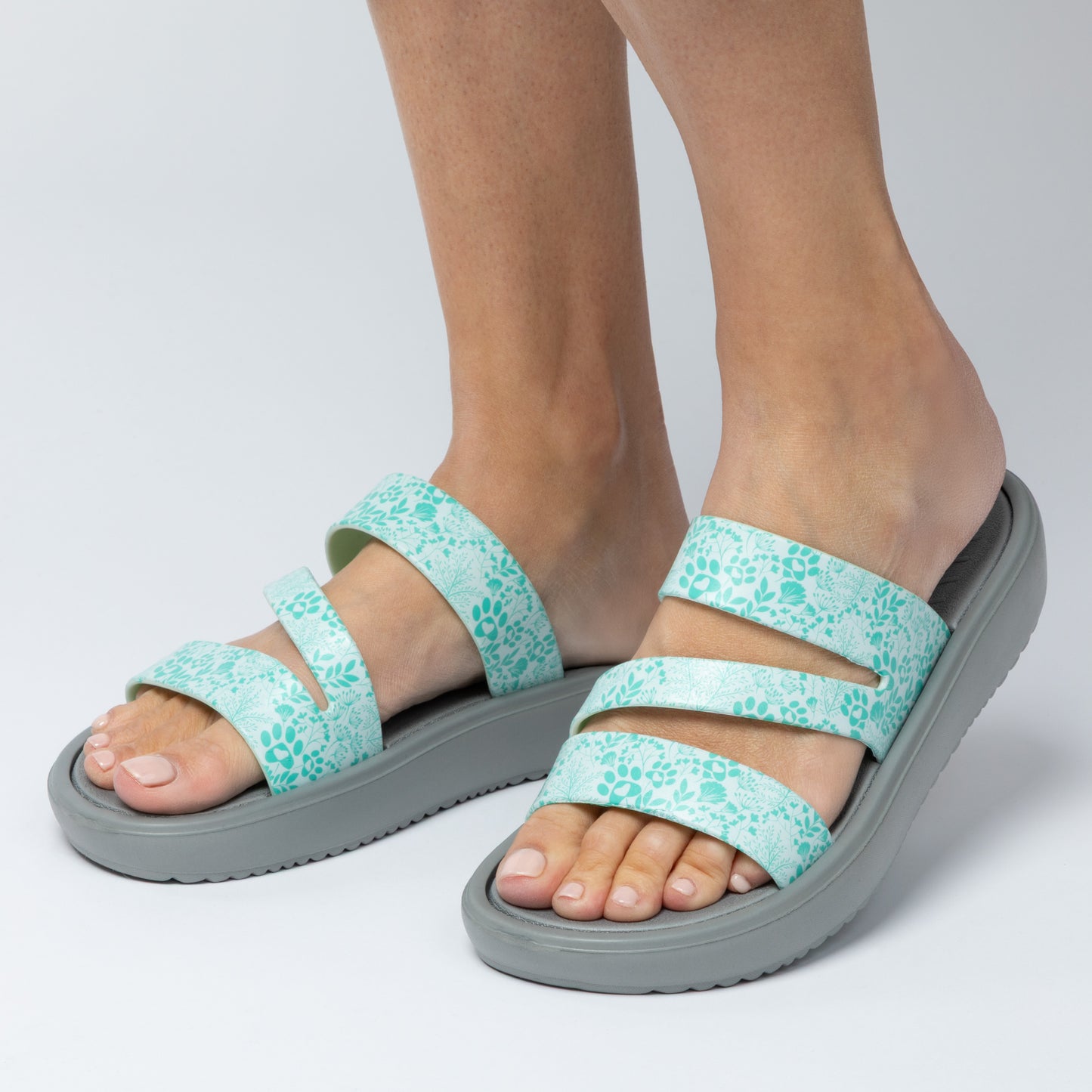 Teal floral sandals with gray soles worn by a person on a light gray background