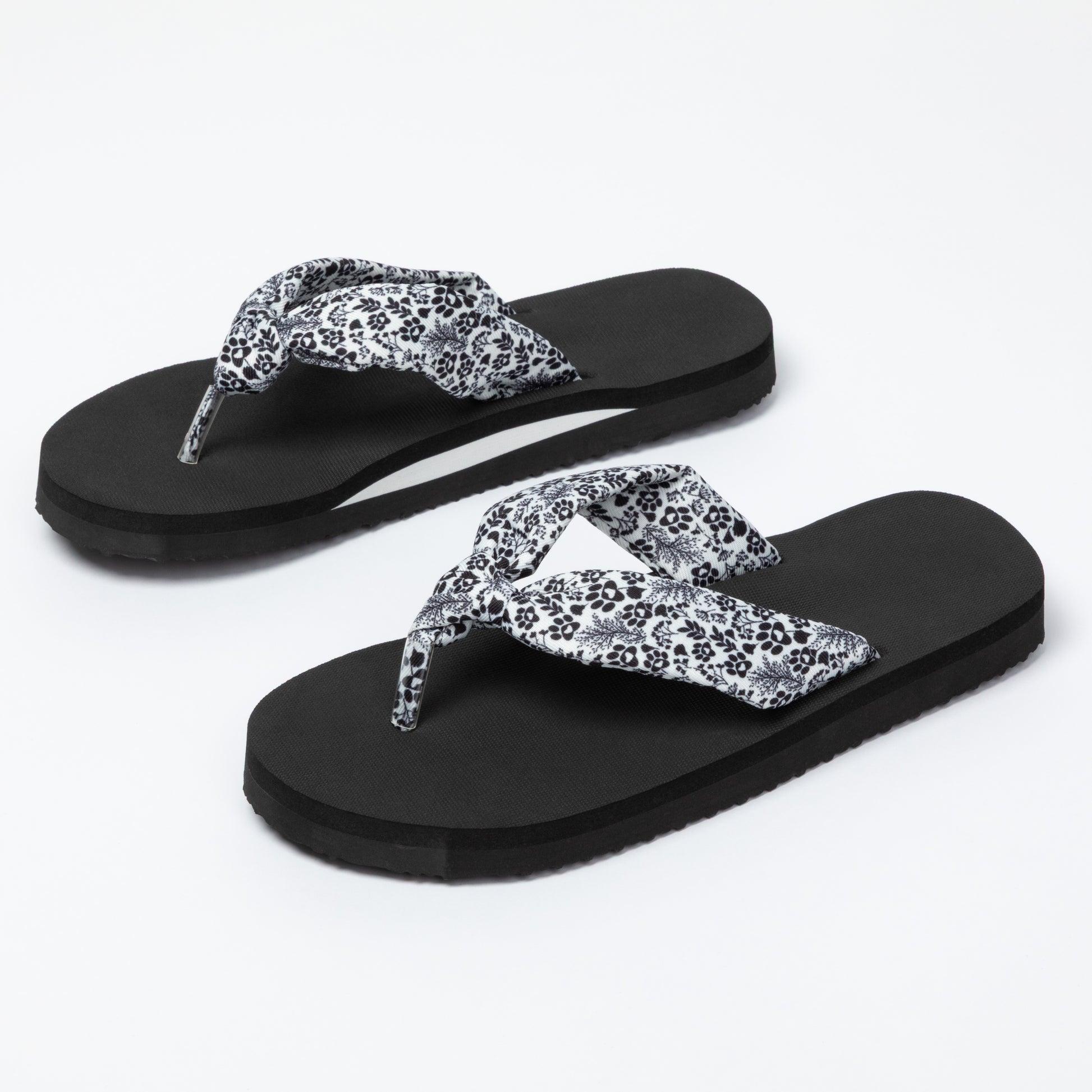 Black flip-flops with white floral patterns on a white background