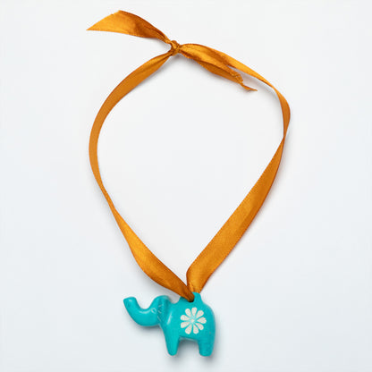 Turquoise elephant soapstone ornament with a white flower on a gold colored ribbon against a light gray background