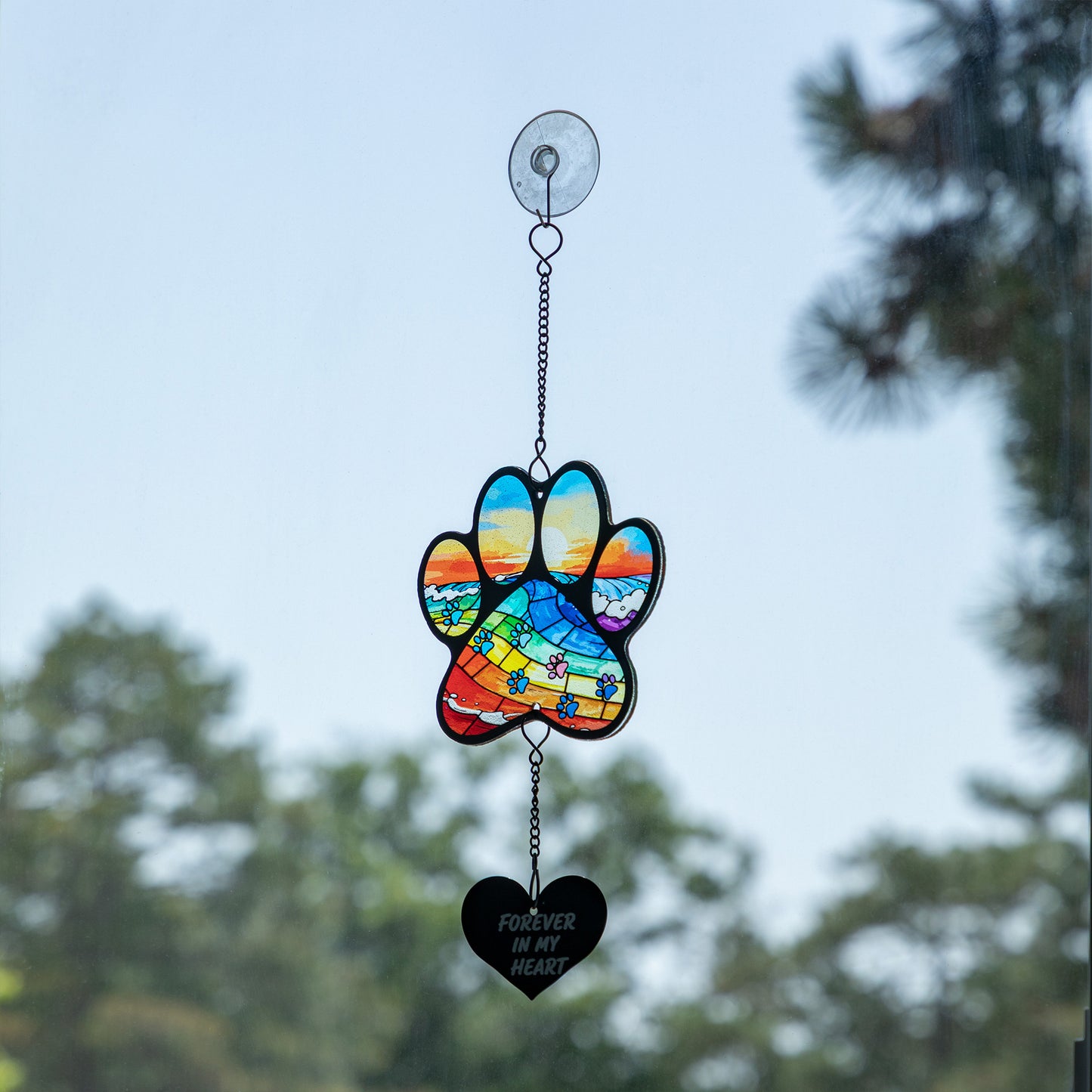 Rainbow bridge stained glass sun catcher with a heart that says "forever in my heart" hanging on a glass window.