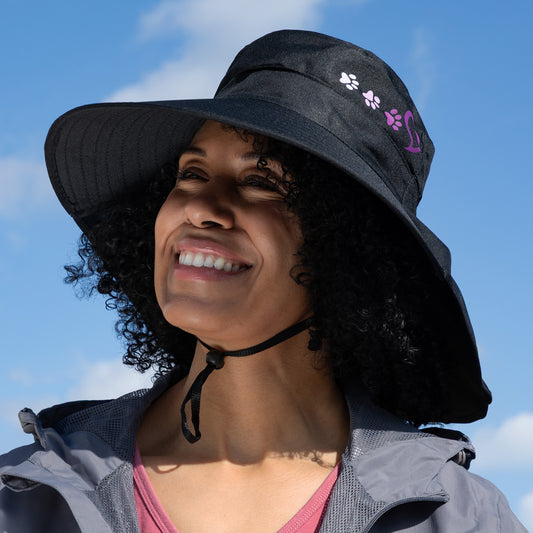 Woman wearing a black sun hat with paw prints against a blue sky.