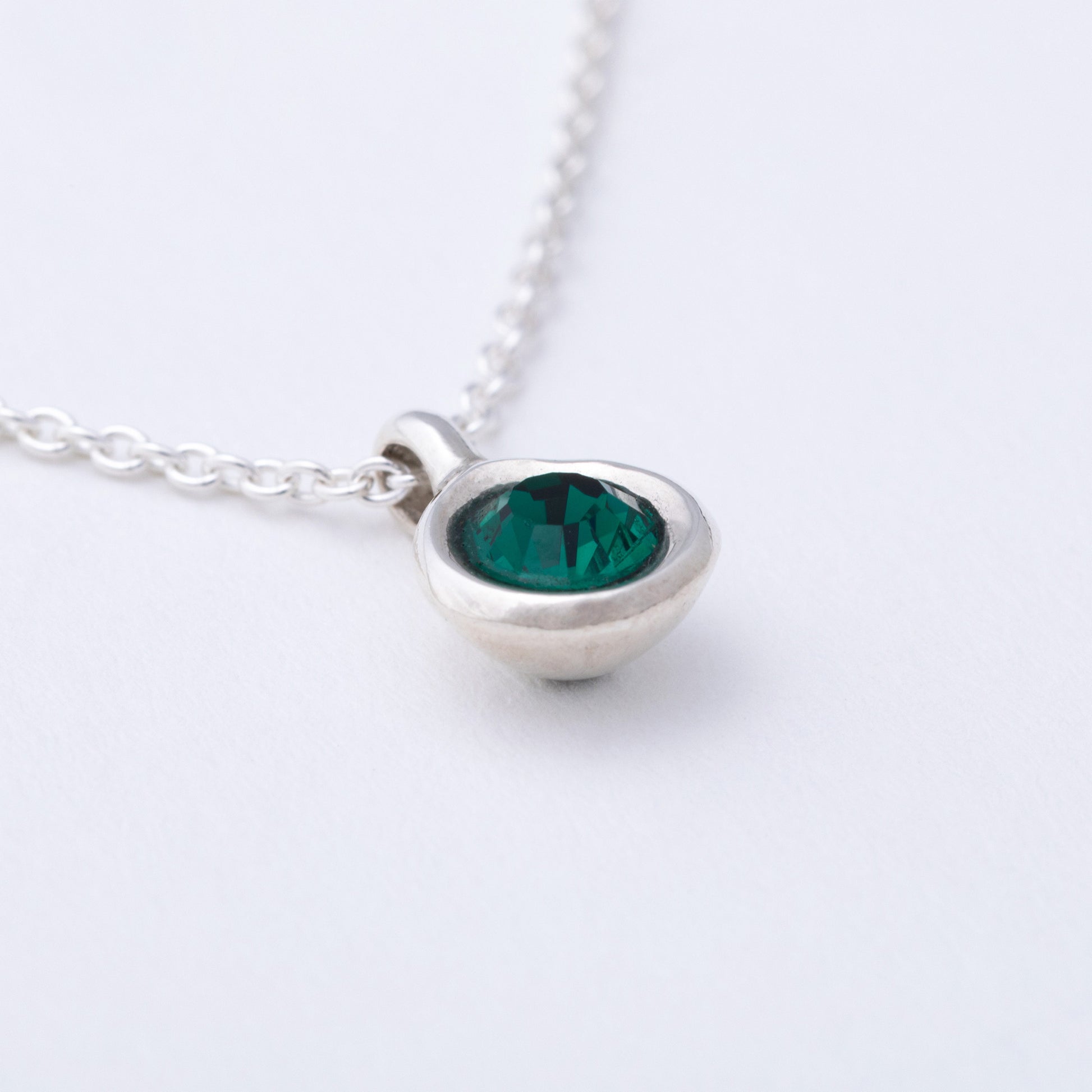 Silver necklace with a green gemstone pendant on a white background