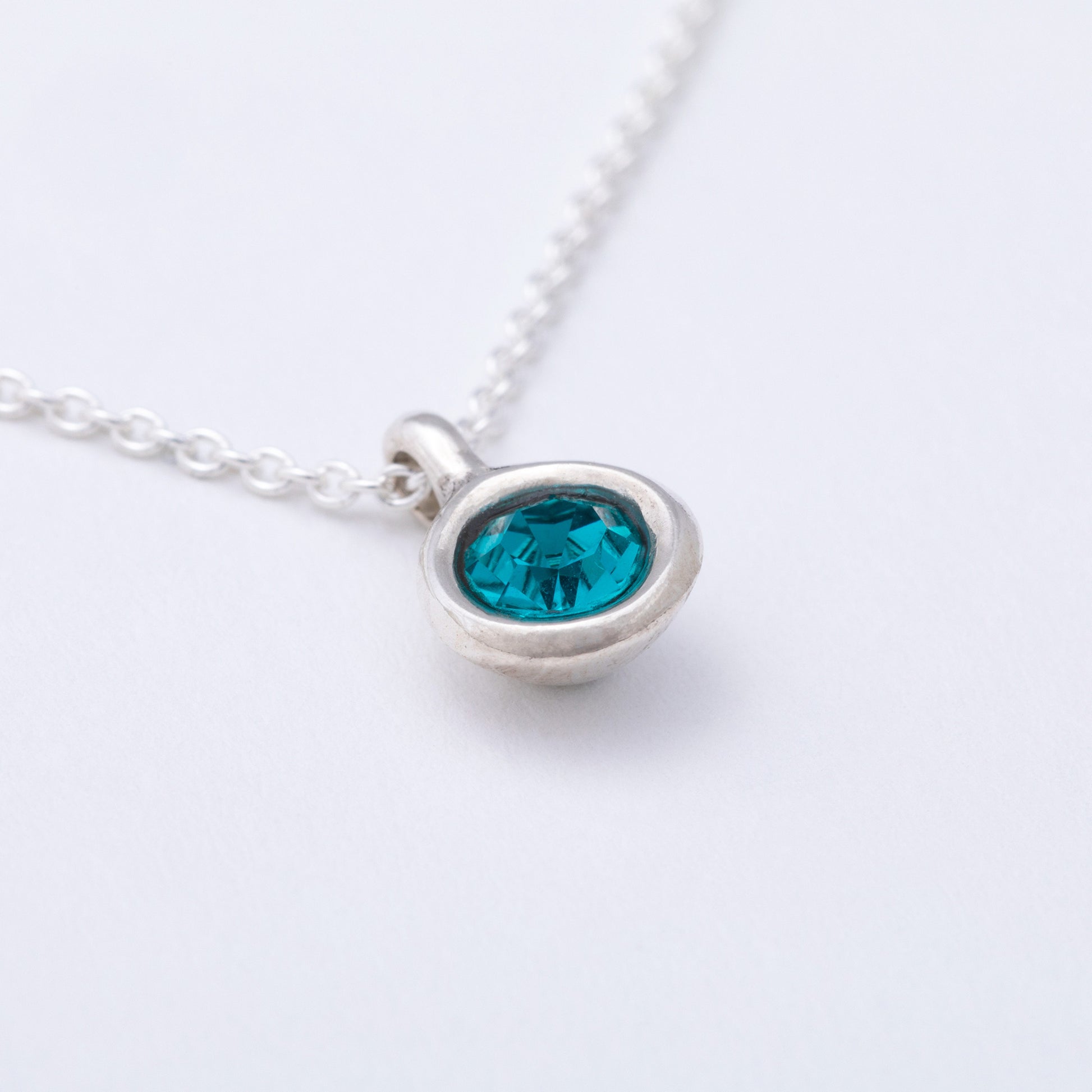 Silver necklace with a blue gemstone pendant on a white background