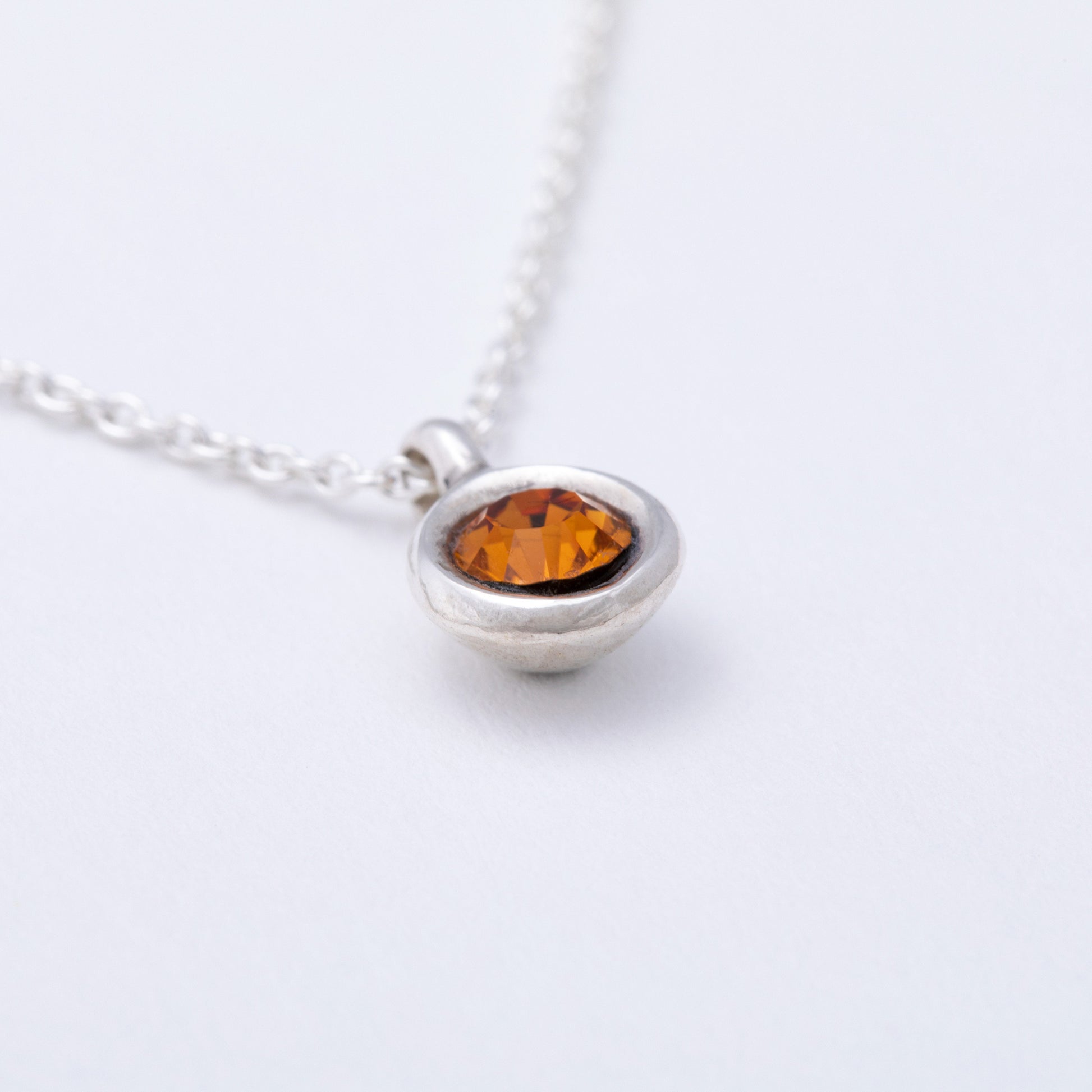 Silver necklace with a round amber stone on a white background