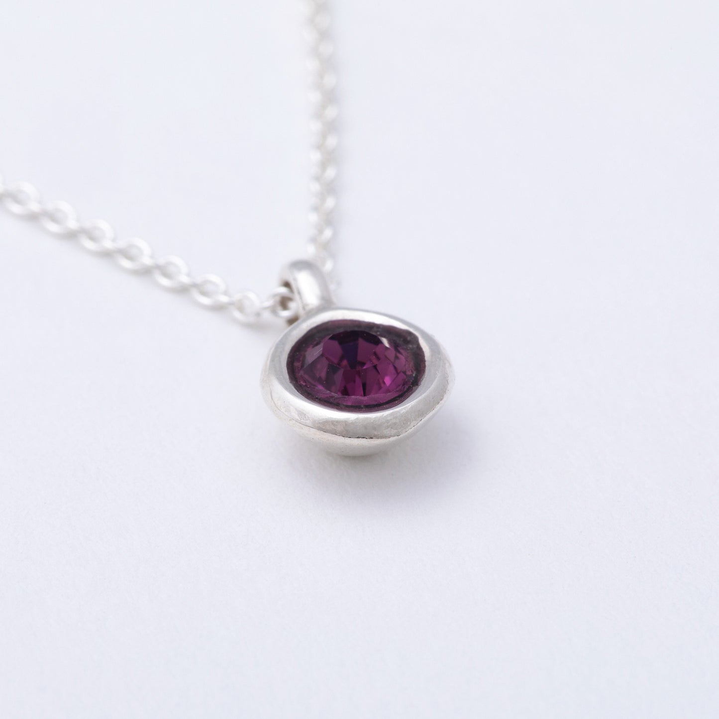 Silver necklace with a purple gemstone on a white background