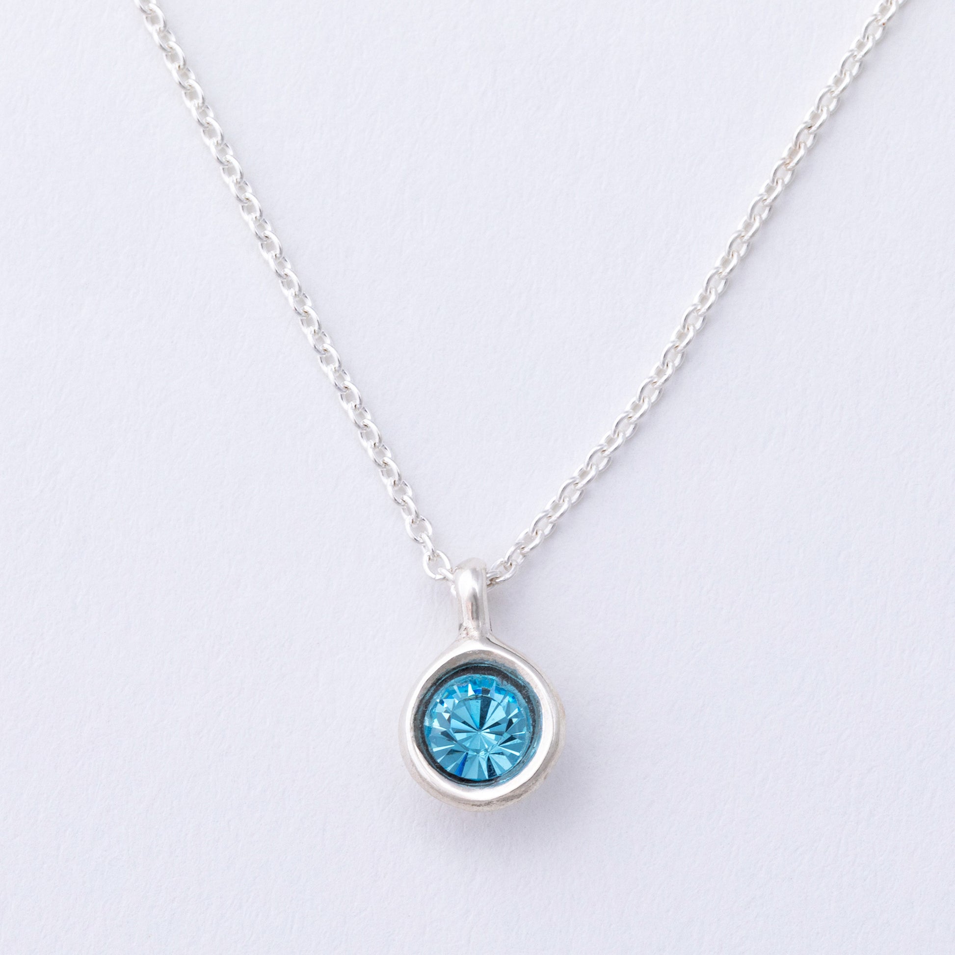 Silver necklace with a blue gemstone pendant on a light gray background