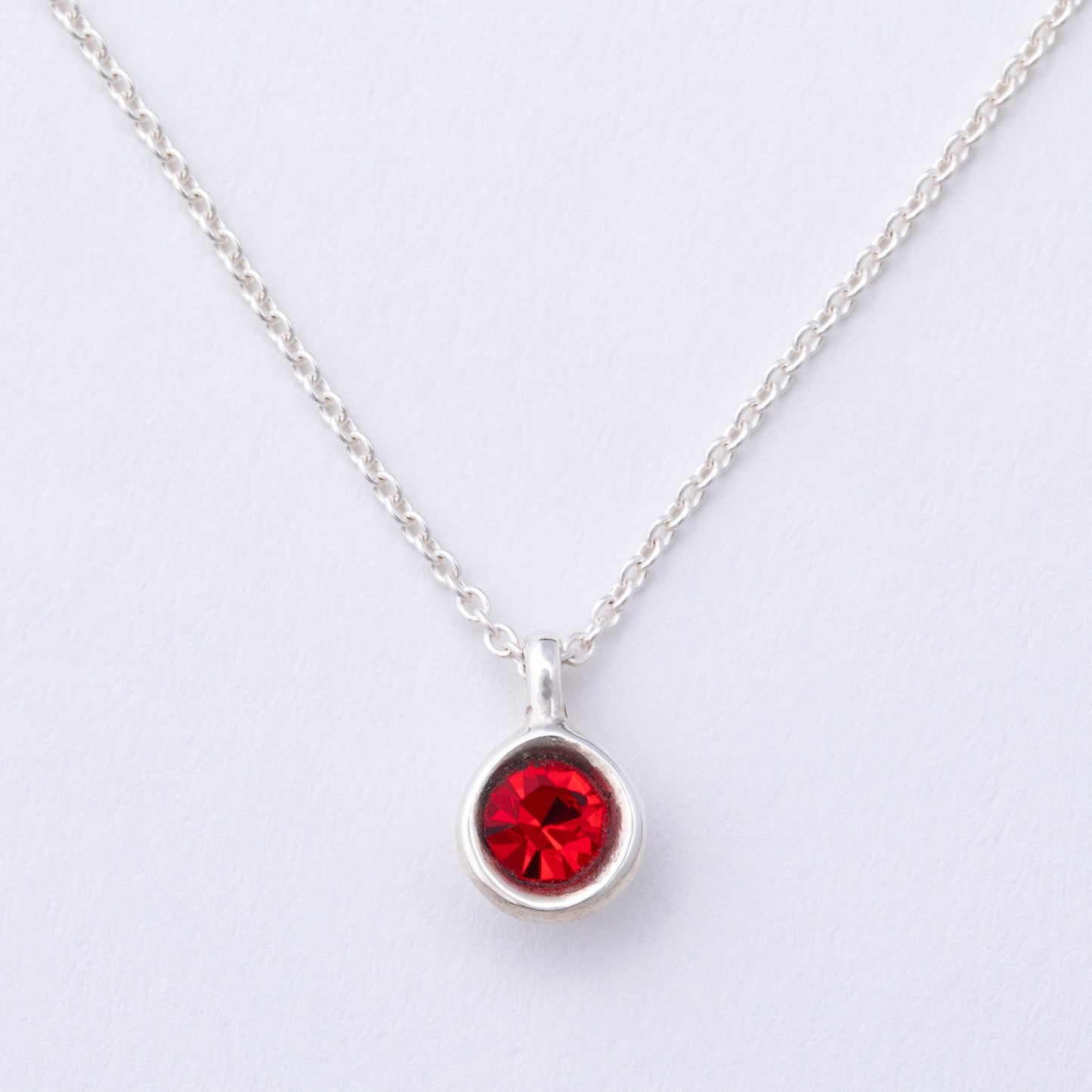 Silver necklace with a red gemstone pendant on a light gray background