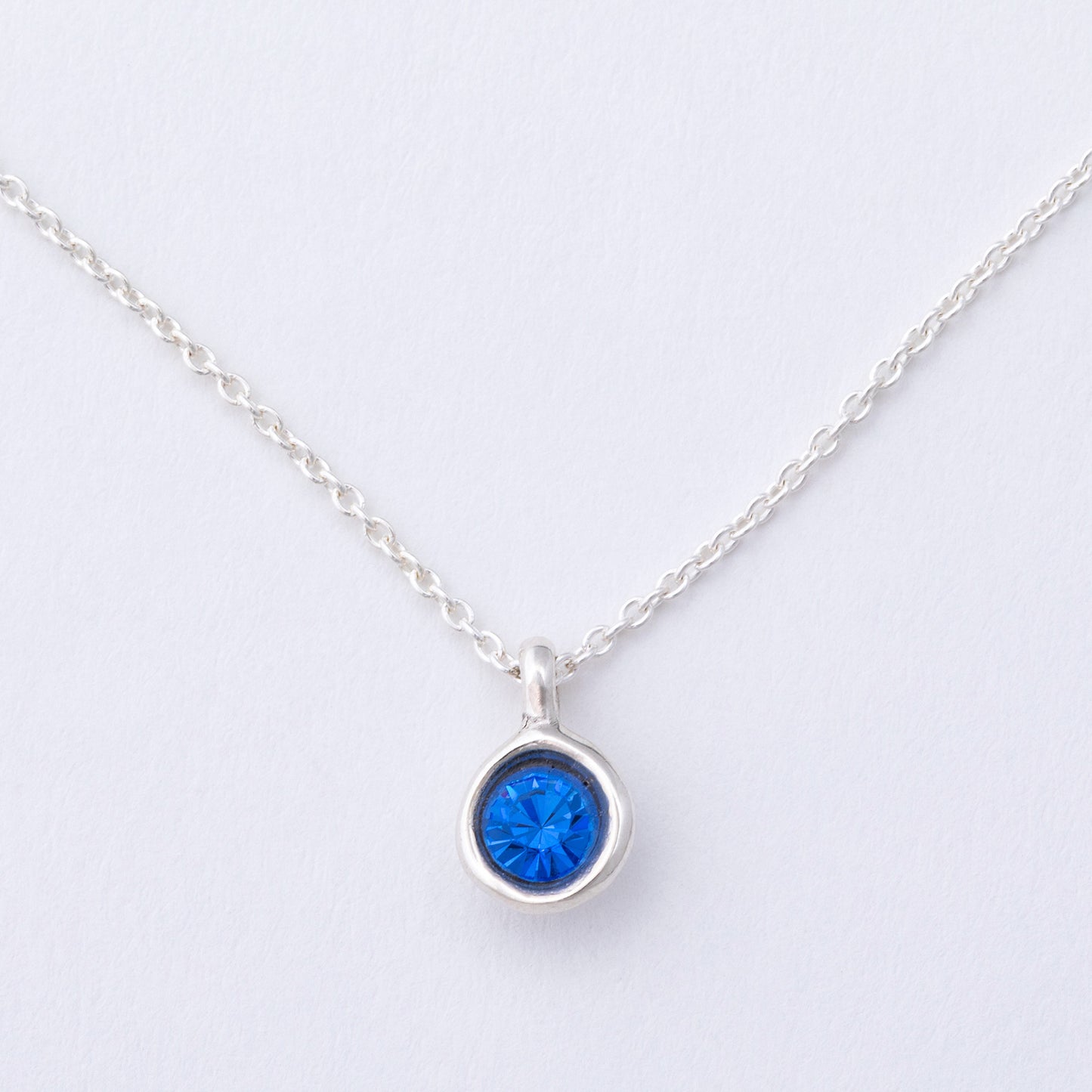 Silver necklace with a blue gemstone pendant on a light gray background