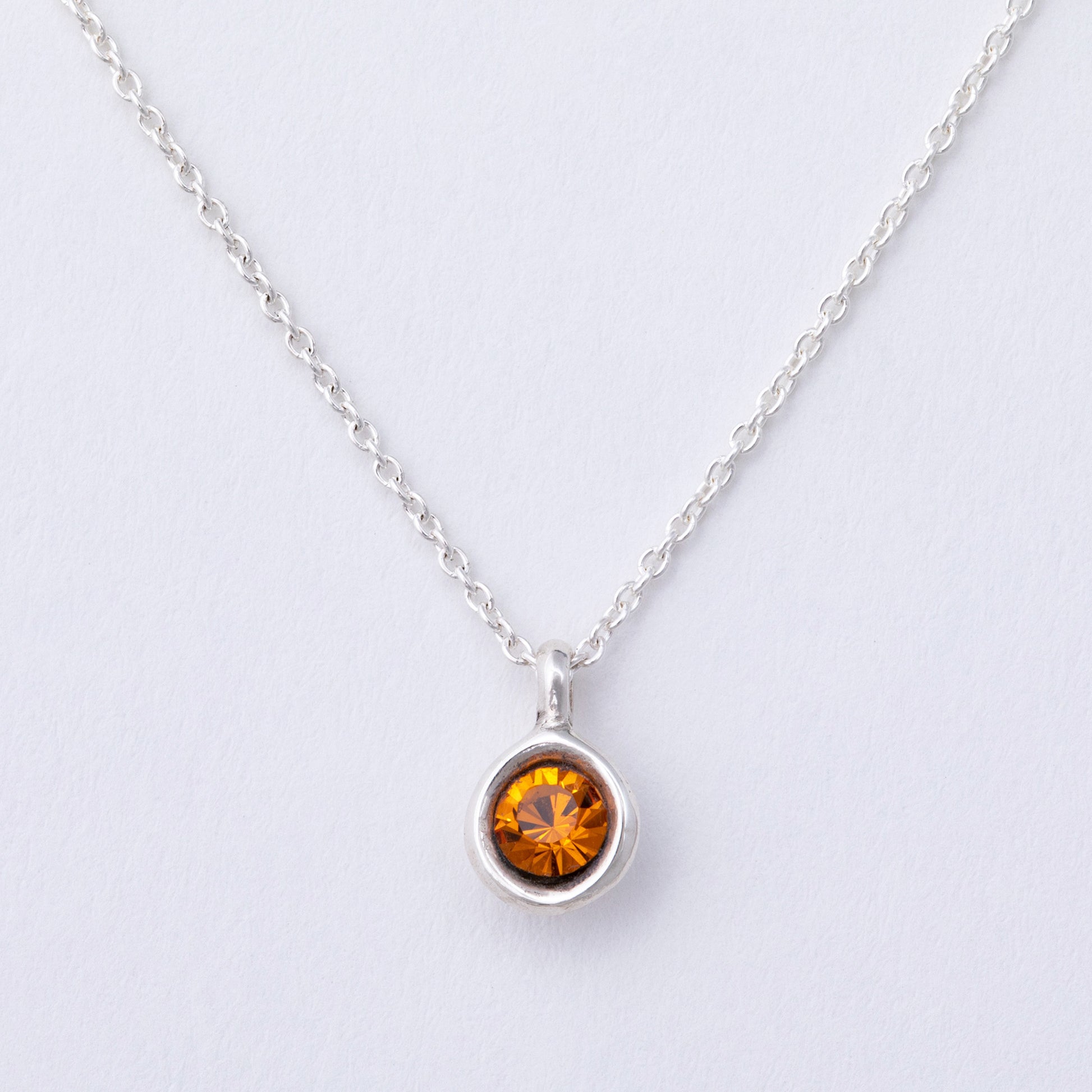 Silver necklace with a round amber-colored gemstone on a light gray background