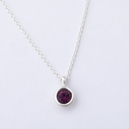 Silver necklace with a purple gemstone pendant on a light gray background