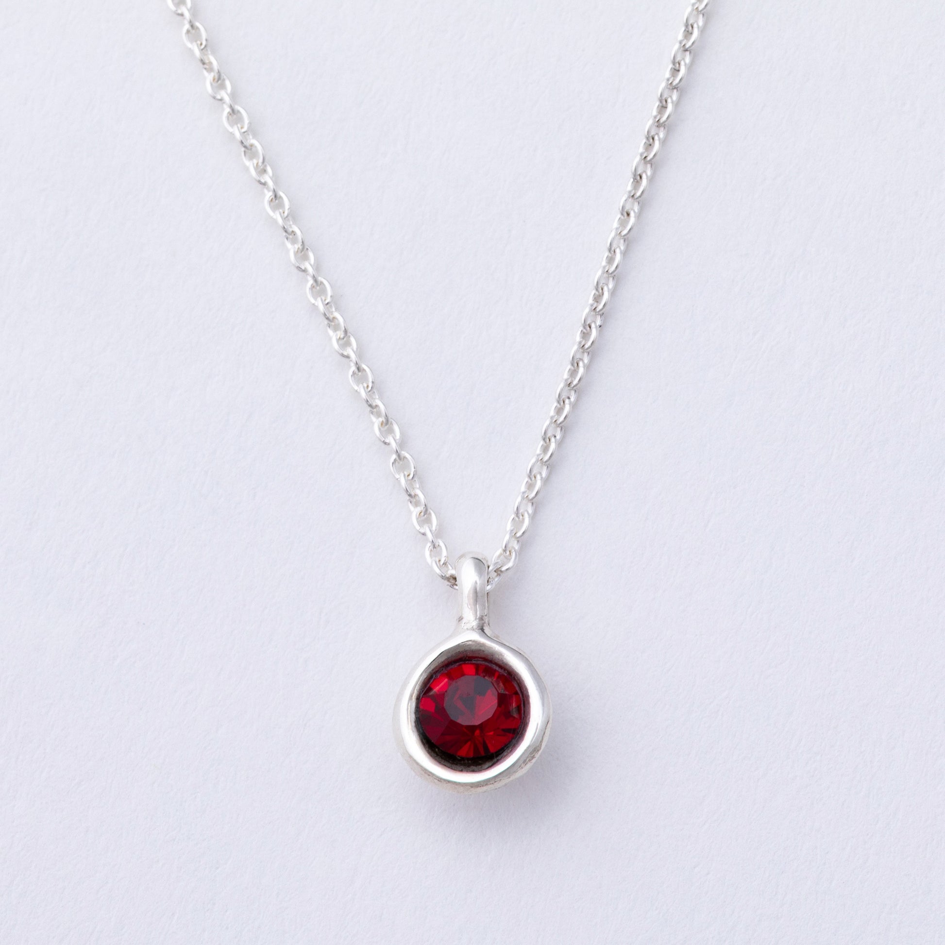 Silver necklace with a red gemstone pendant on a light gray background