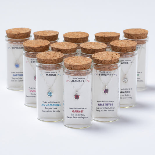 Jars with cork lids containing jewelry and birthstone information on a white background