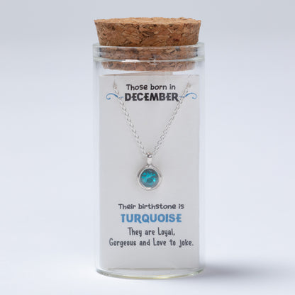 Necklace in a glass jar with a cork lid, featuring information about December-born individuals and their birthstone.