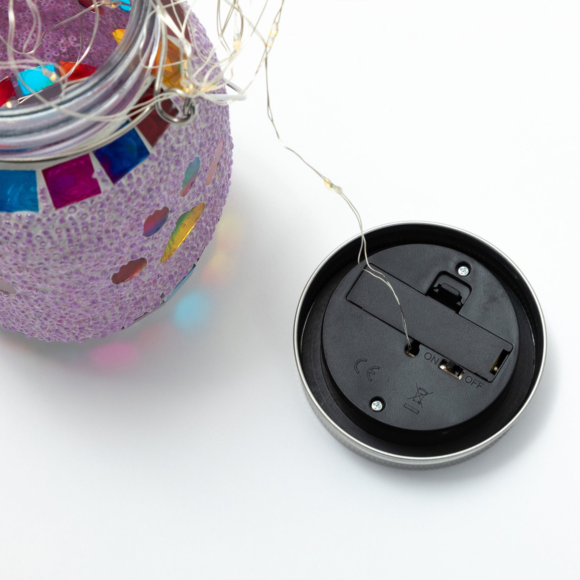 Close-up of a decorative solar lantern jar with colorful mosaic and a black lid on a white background.