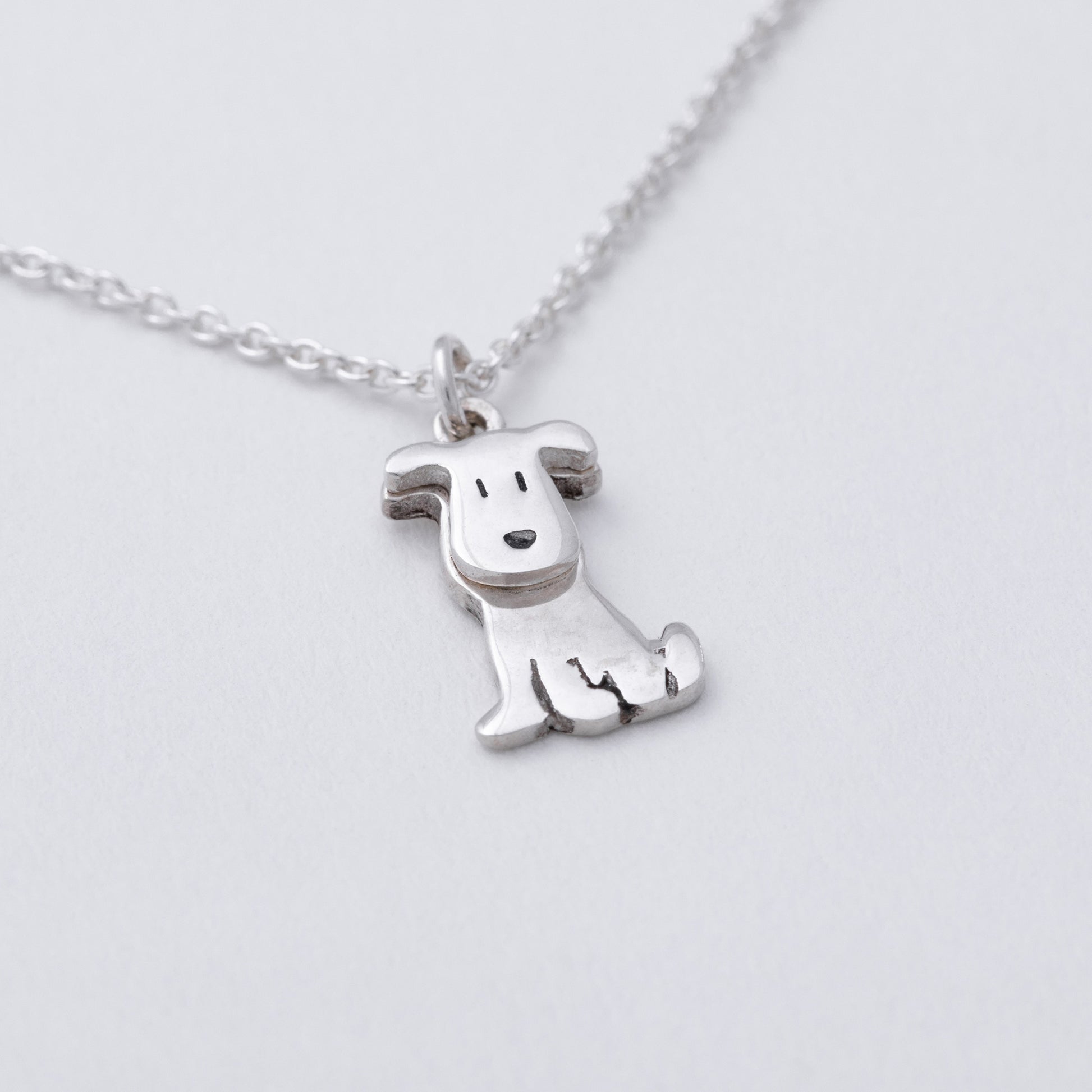 Silver dog-shaped pendant on a chain against a light gray background