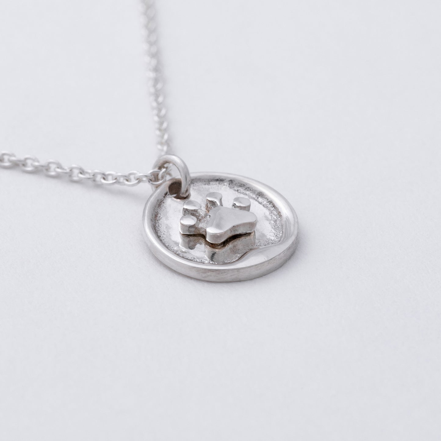 Sterling silver circular pendant with a small paw print on it, against a white background.