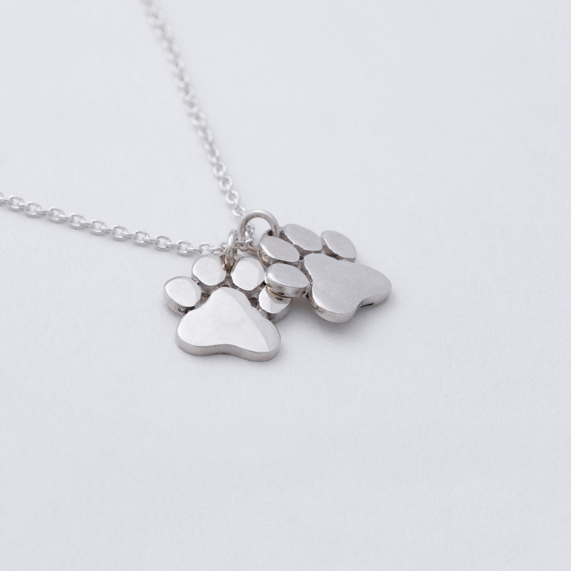 Silver necklace with paw-shaped pendants on a light gray background