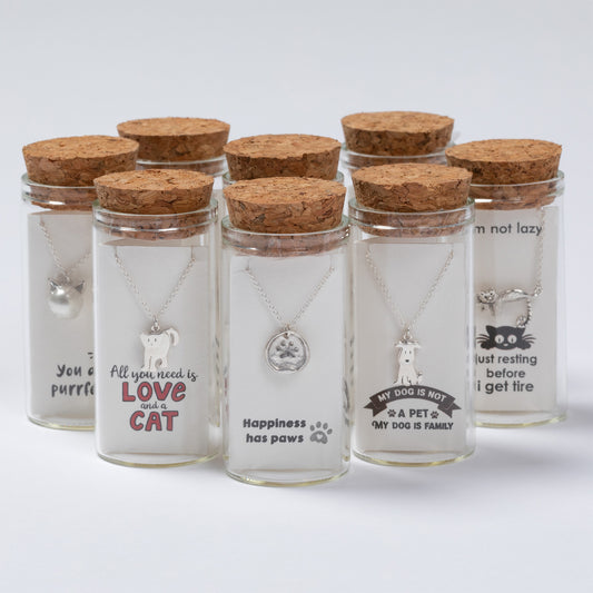 Set of glass jars with cork lids containing pet-themed necklaces on a white background