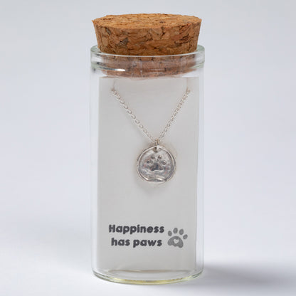 Glass jar with cork lid containing a necklace with a paw print pendant, on a light gray background.
