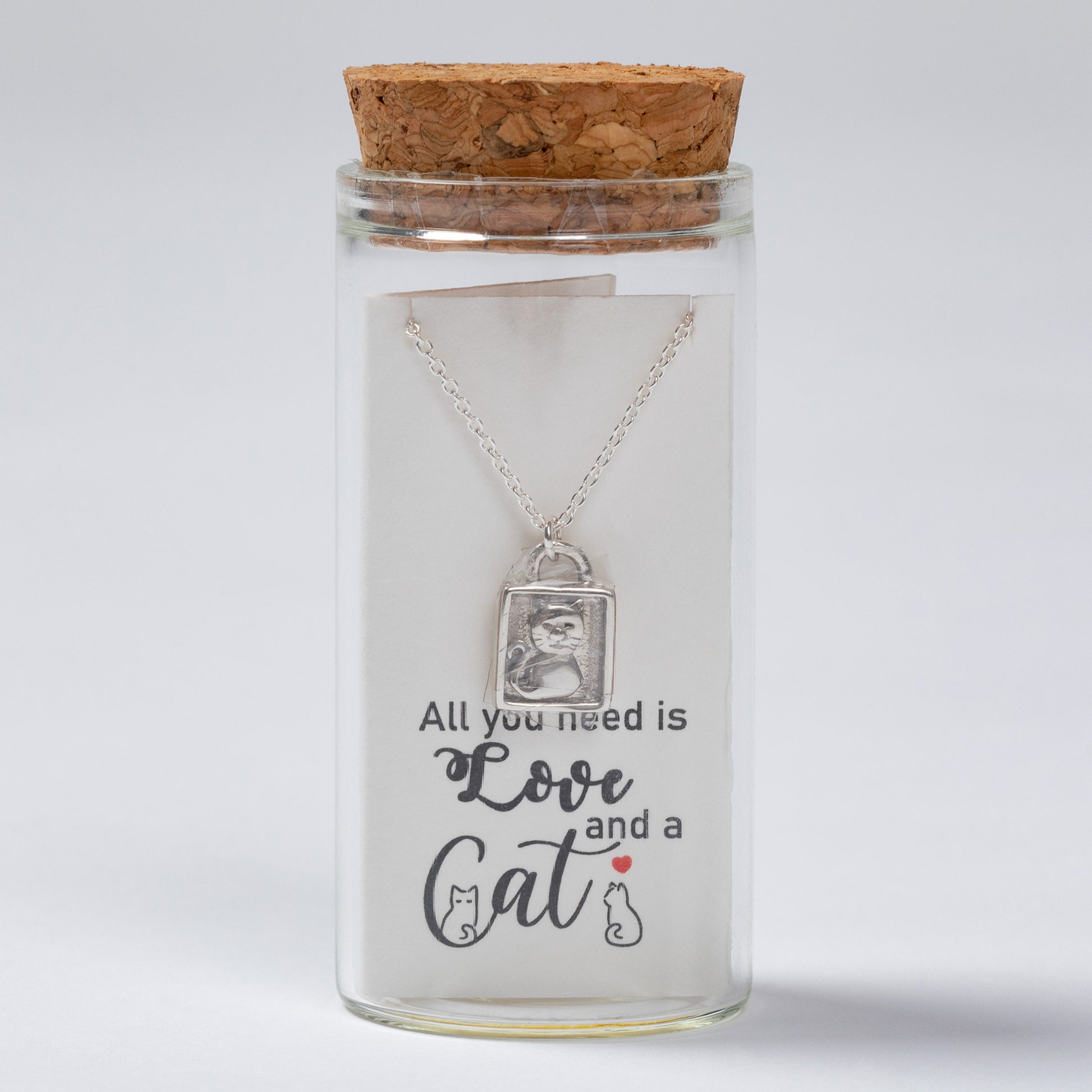 Glass jar with cork lid containing a necklace with a cat-themed pendant and text 'All you need is love and a cat'.