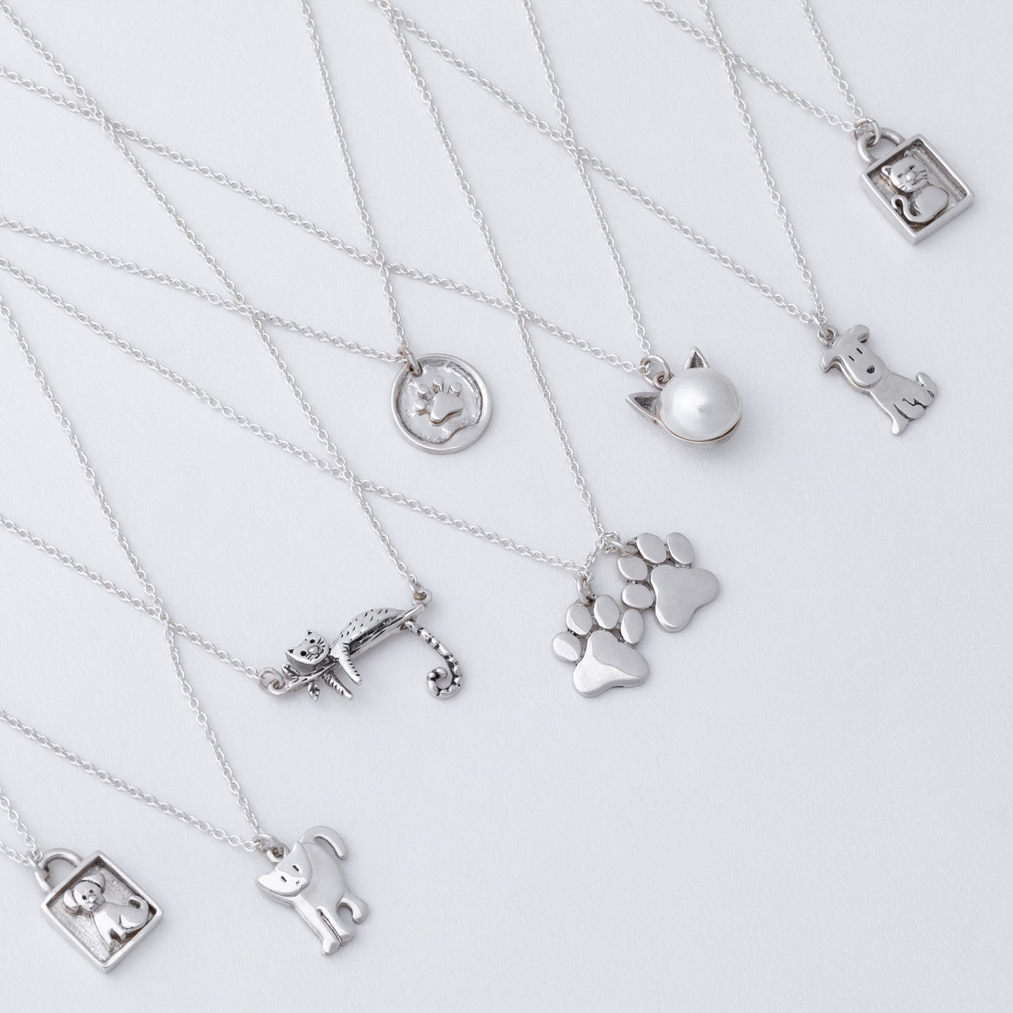Collection of silver necklaces with various pendants on a light gray background