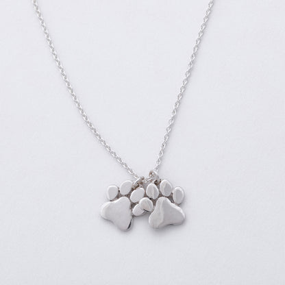 Silver necklace with paw-shaped pendants on a light gray background