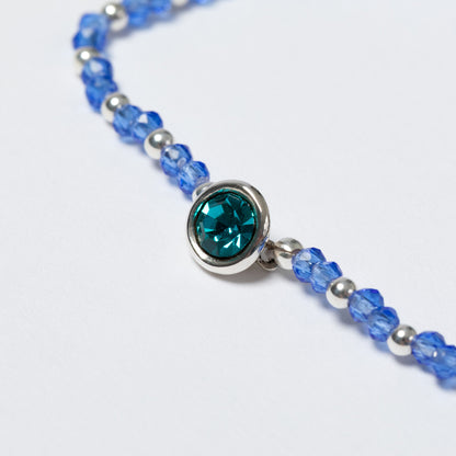 Bracelet with blue beads and a central teal gemstone on a white background