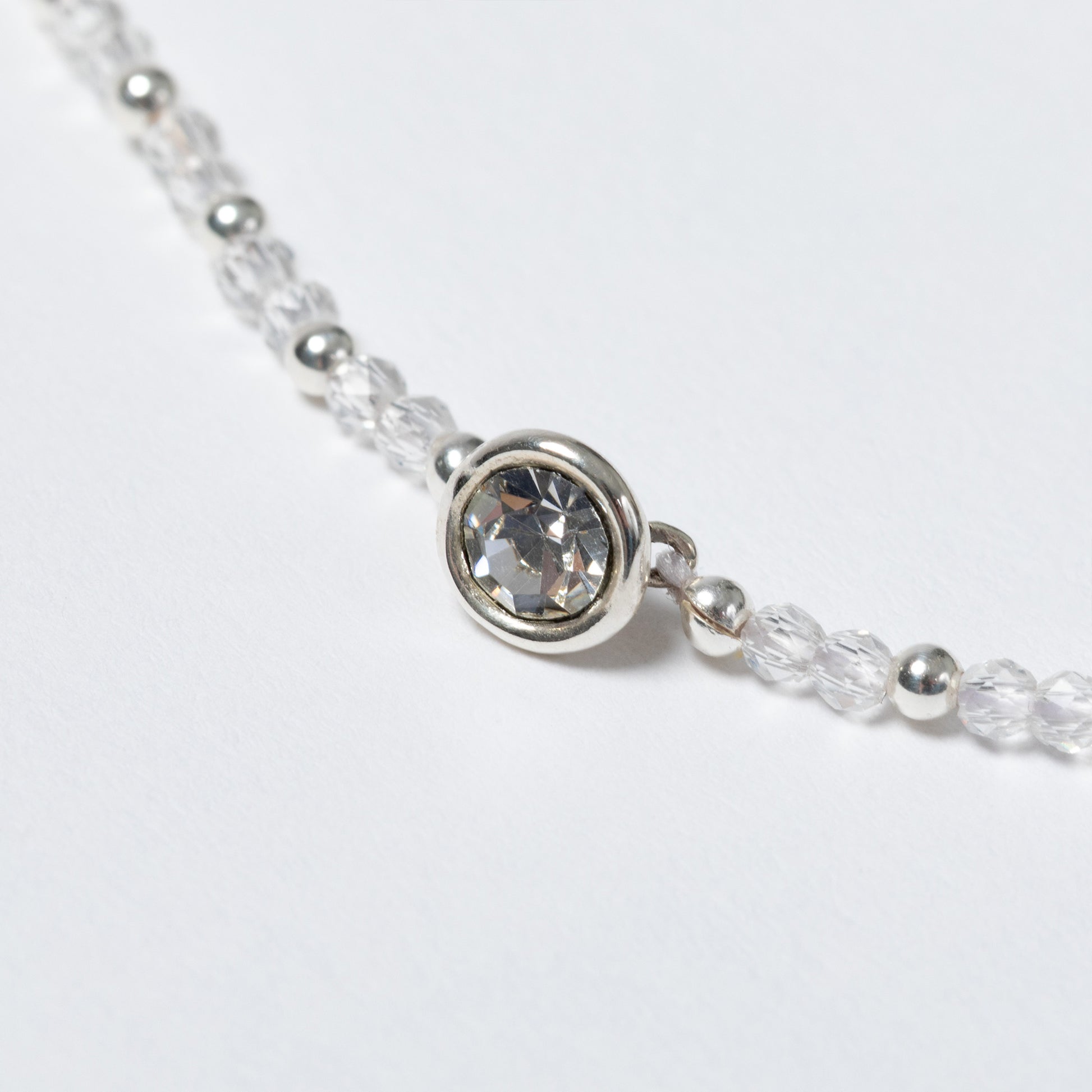 Close-up of a silver beaded necklace with a clear gemstone on a light gray background