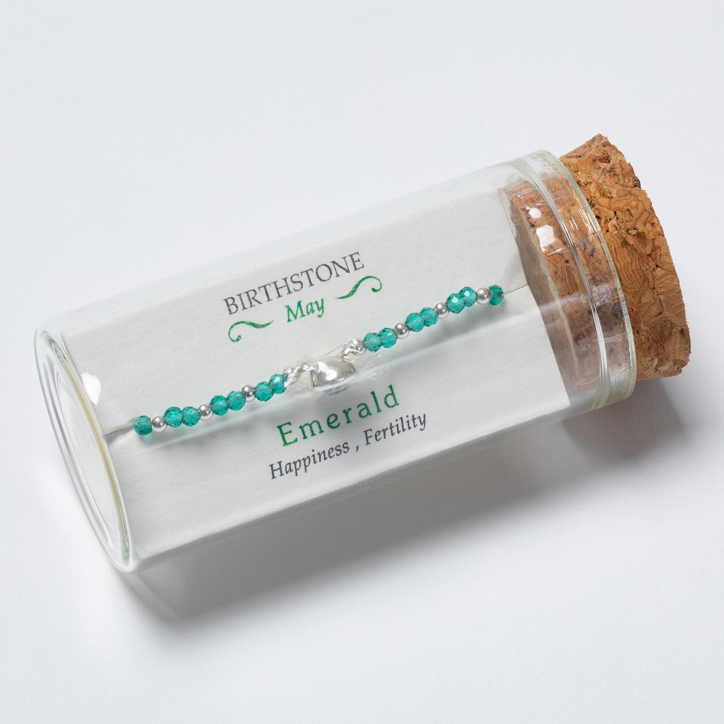 Emerald birthstone bracelet in a glass bottle with cork lid on a white background